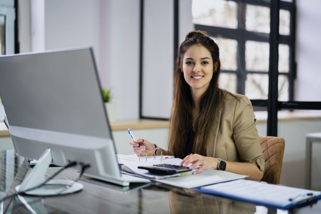 A bookkeeper working at her desk with a calculator and financial documents